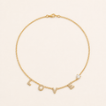 Gold LOVE letter zircon necklace on a warm cream background